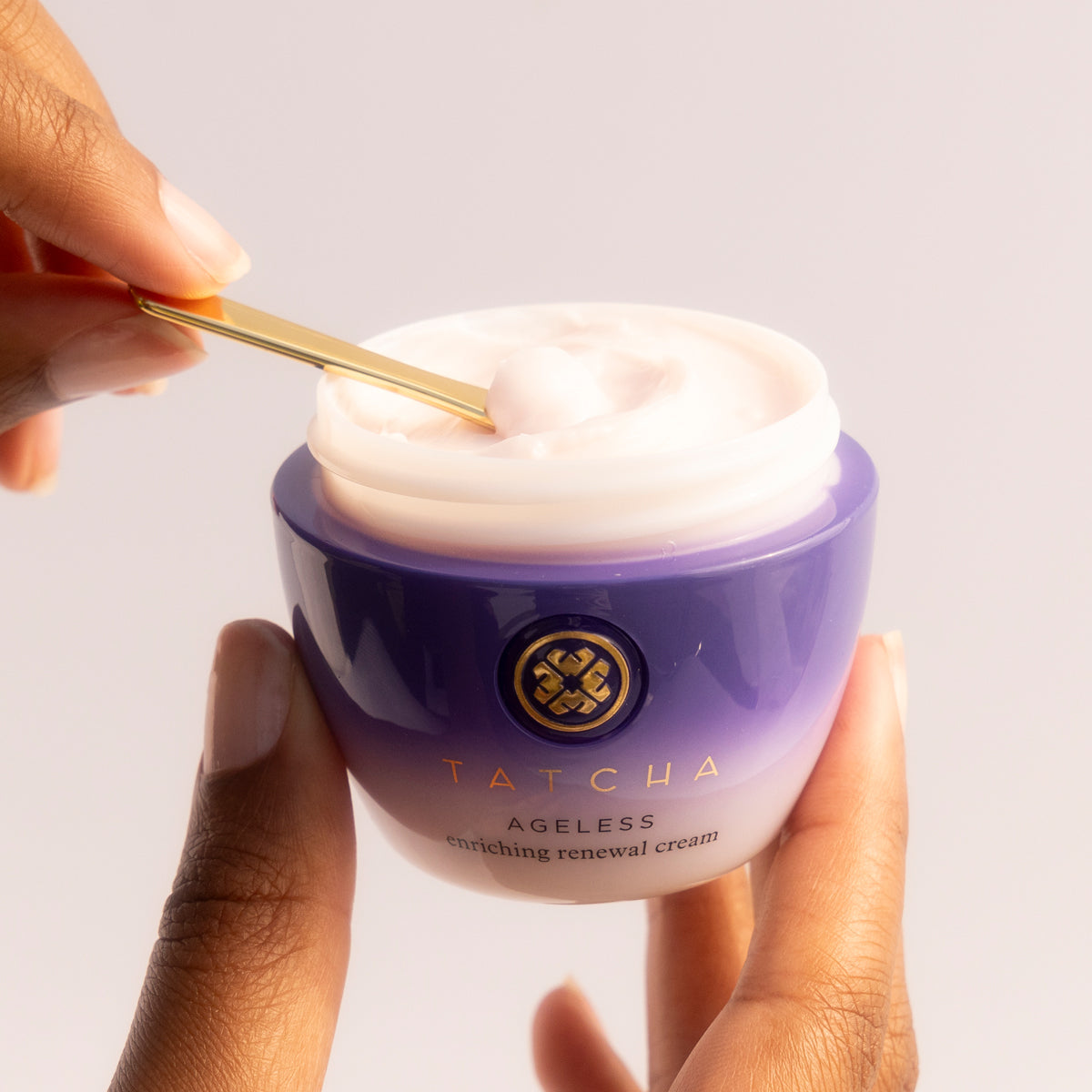 Hand holding Ageless Enriching Renewal Cream with other hand scooping